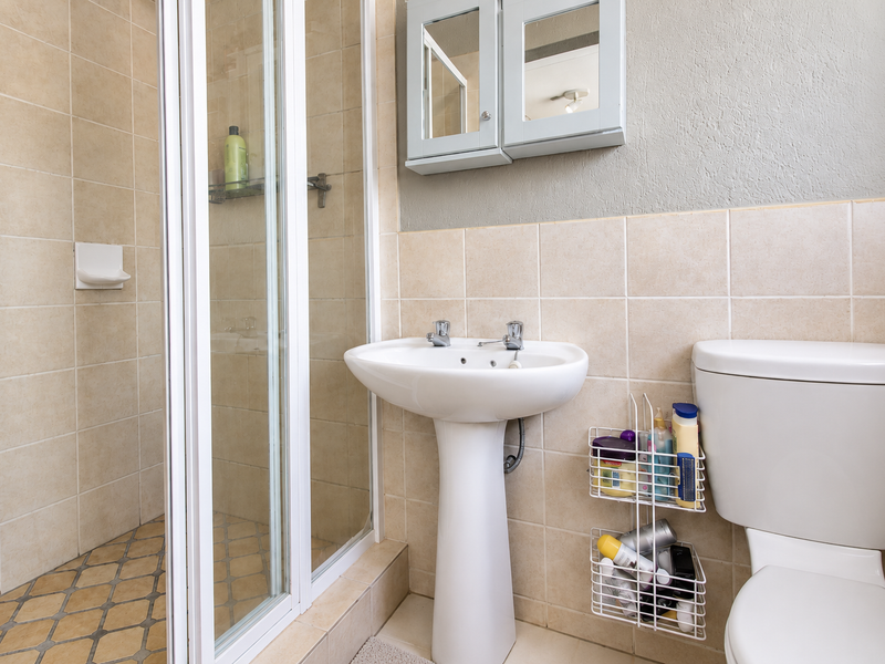 A functional bathroom featuring a pedestal basin, a shower enclosure with tiled walls, and a wall-mounted medicine cabinet.