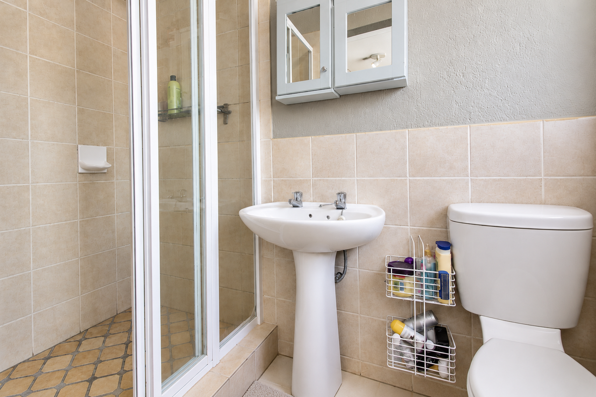 A functional bathroom featuring a pedestal basin, a shower enclosure with tiled walls, and a wall-mounted medicine cabinet.
