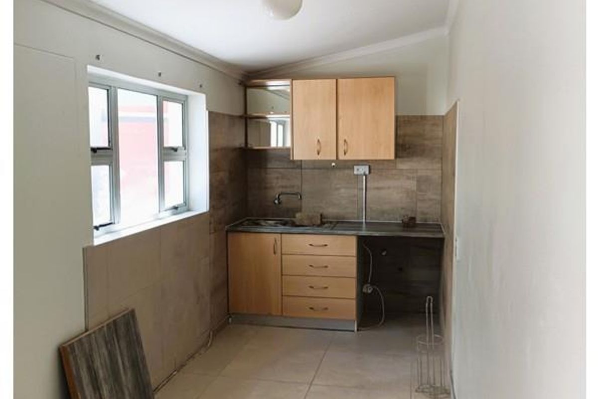 A compact kitchenette featuring light wood cabinetry, tiled splashbacks, and tiled flooring, offering a functional space for office staff.