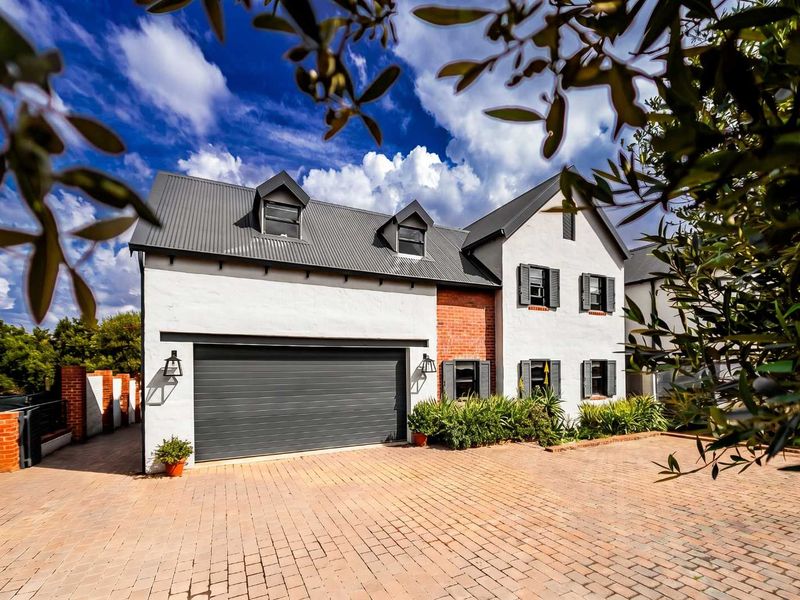 A well-maintained double-story home featuring a brick-paved driveway, a double garage, and a classic architectural design with dormer windows and shuttered accents.