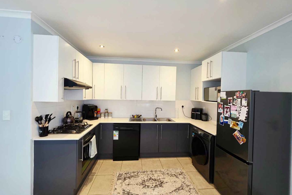 Modern U-shaped kitchen featuring white upper cabinetry, dark lower cabinets, integrated gas hob, extractor fan, and tiled flooring.
