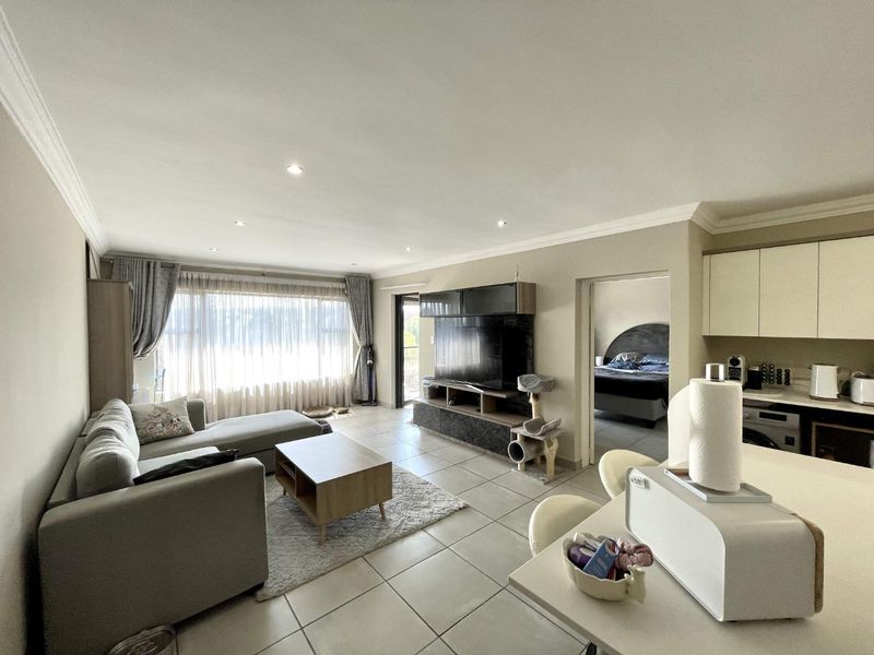 Open-plan living area featuring tiled floors, recessed lighting, and a seamless transition between the kitchen and lounge space with access to a balcony.