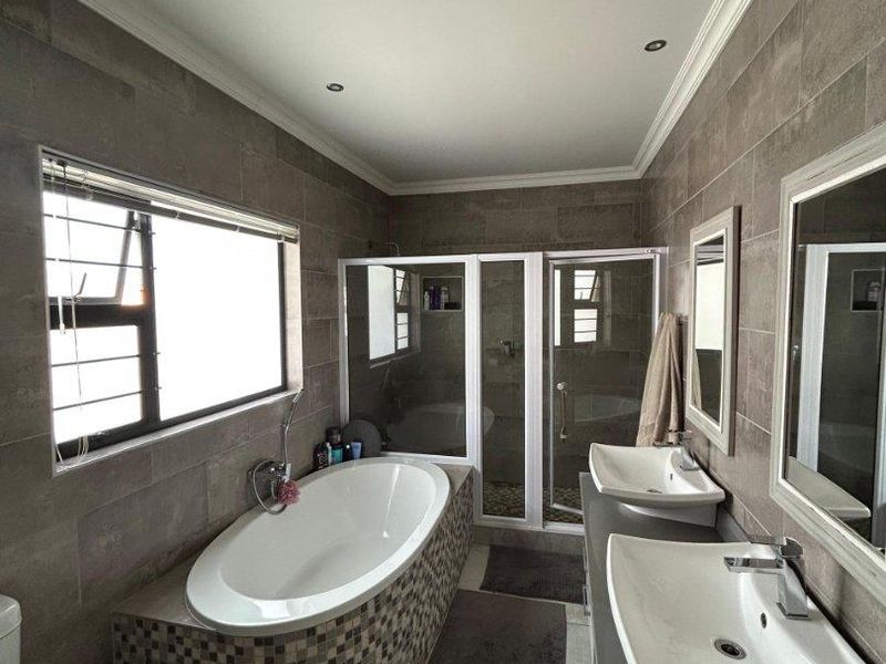 Modern bathroom featuring a double vanity, a tiled freestanding bathtub, and a separate glass-enclosed shower with neutral wall and floor tiling.