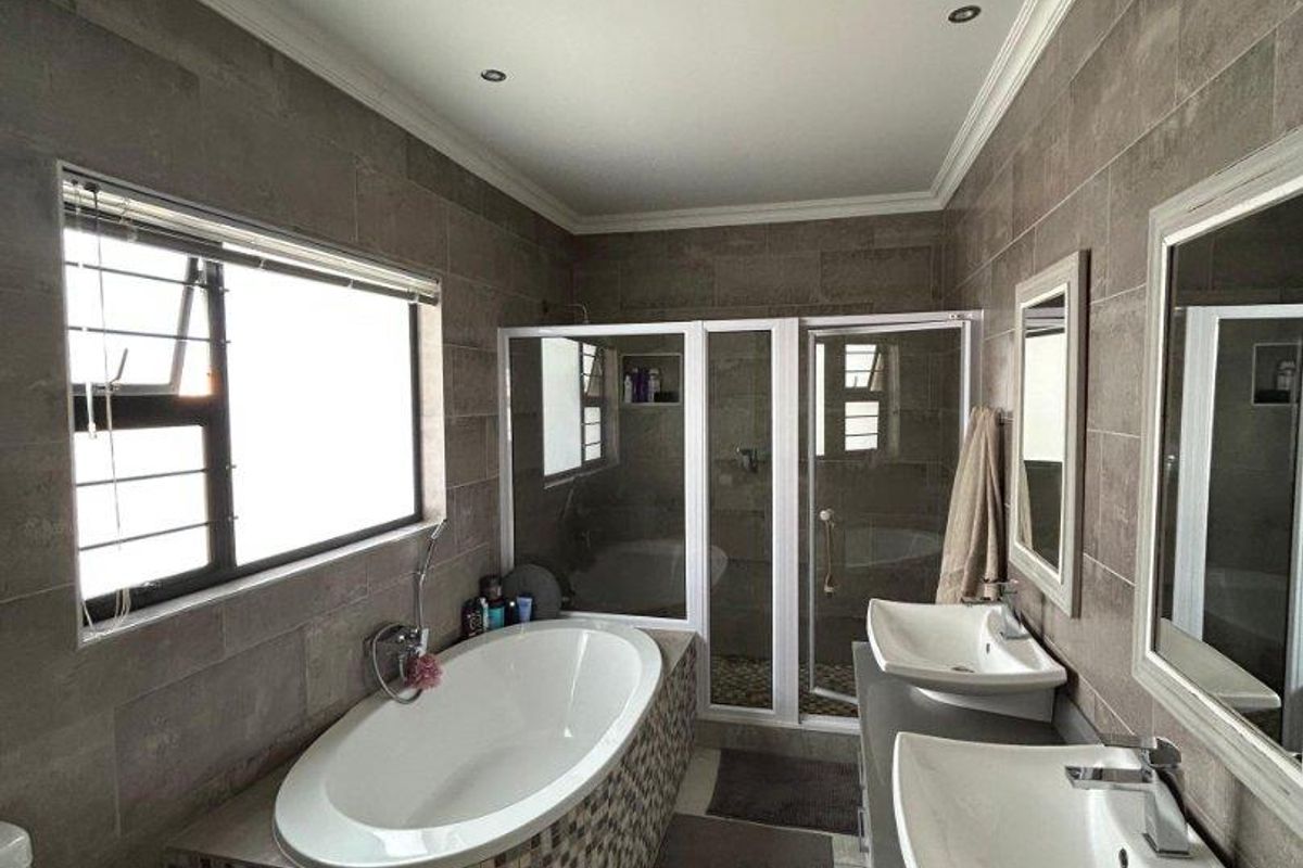 Modern bathroom featuring a double vanity, a tiled freestanding bathtub, and a separate glass-enclosed shower with neutral wall and floor tiling.