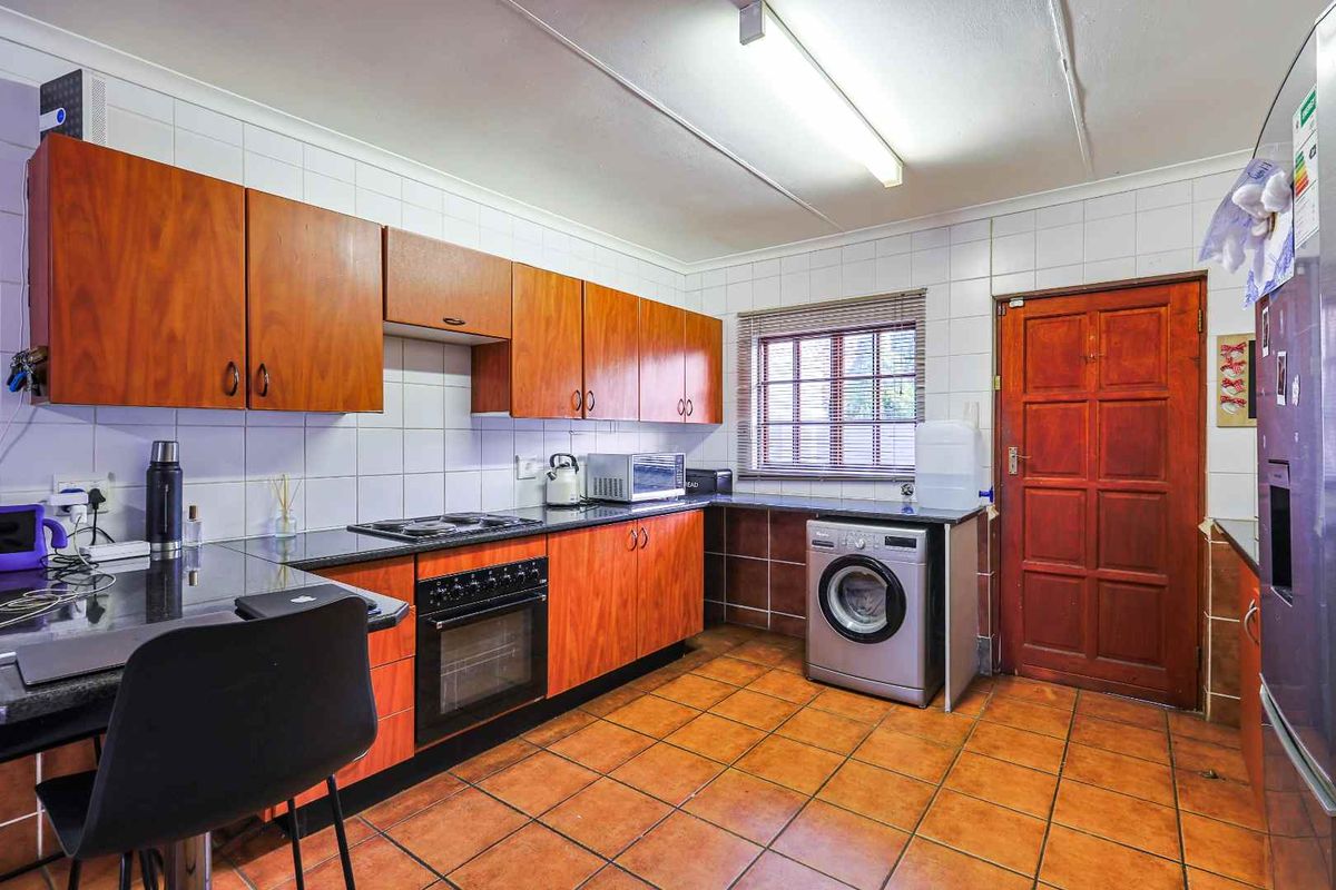 Functional kitchen featuring wood-look cabinetry, dark countertops, integrated oven and hob, tiled splashbacks, and dedicated space for laundry appliances.