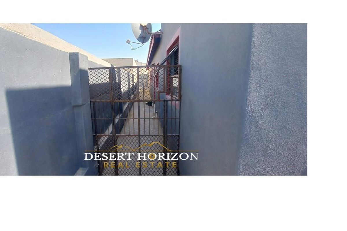 A narrow side passage of the house featuring a metal security gate and exterior wall access.