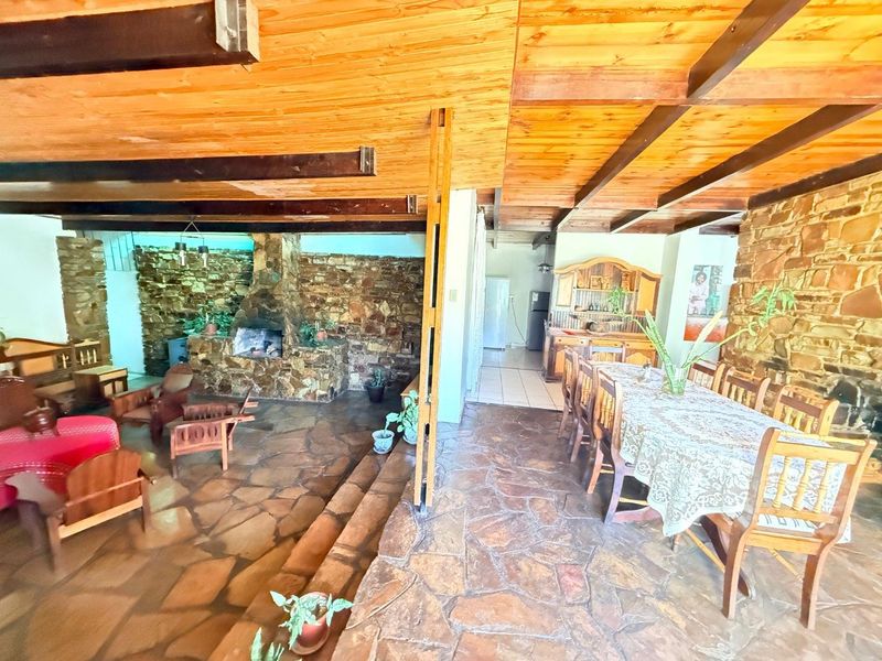 Spacious open-plan living and dining area featuring rustic flagstone flooring, exposed timber ceiling beams, and a prominent stone fireplace.
