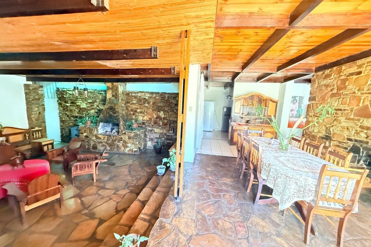 Spacious open-plan living and dining area featuring rustic flagstone flooring, exposed timber ceiling beams, and a prominent stone fireplace.