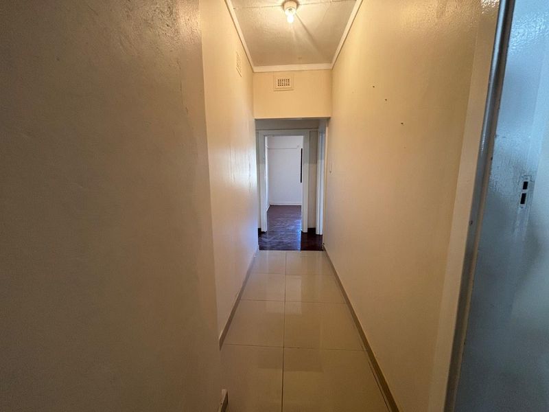 A functional, empty hallway featuring neutral tiled flooring and simple ceiling lighting, providing access to adjacent rooms.