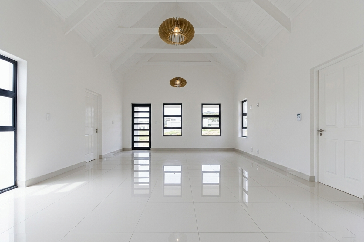 Spacious, light-filled living area featuring high vaulted ceilings with exposed beams, polished porcelain floor tiles, and modern black-framed windows and doors.