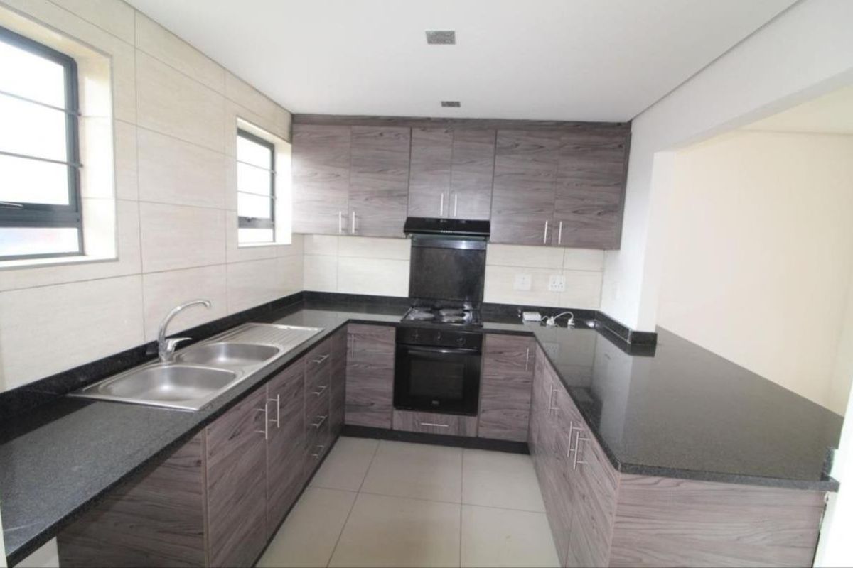 A modern, well-maintained kitchen featuring dark wood-grain cabinetry, granite countertops, a double sink, and built-in oven with gas hob.