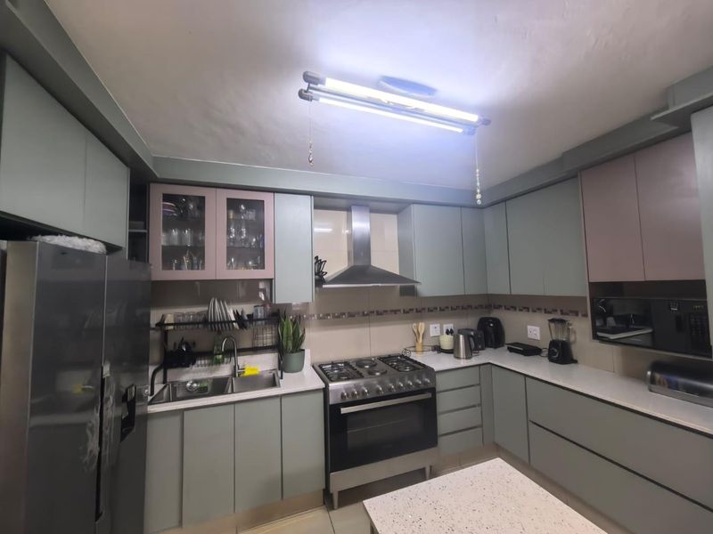 A functional kitchen featuring modern sage green cabinetry, stone countertops, a stainless steel gas stove with extractor fan, and a double sink.