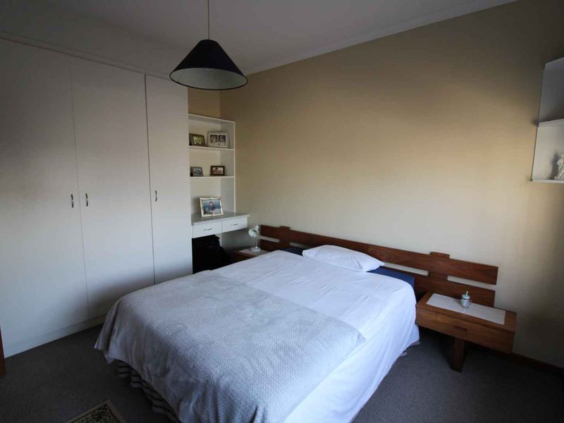 A functional bedroom featuring built-in wardrobes, integrated shelving, a desk area, and floating bedside tables with neutral wall finishes.