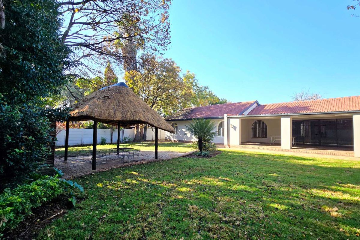 Spacious rear garden featuring a traditional thatched lapa, a covered patio area, and well-maintained lawn, ideal for outdoor entertaining.