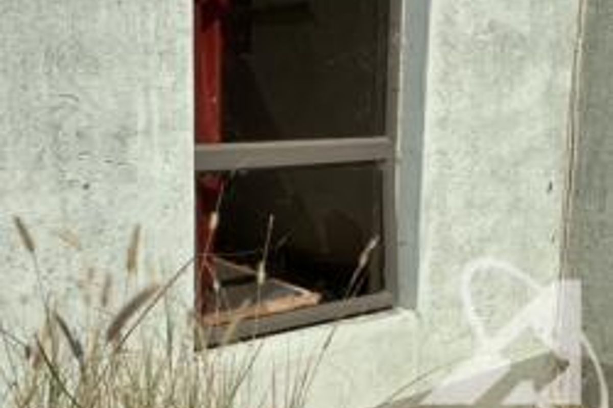 Close-up view of an exterior wall section featuring a damaged window with a broken pane and compromised frame.