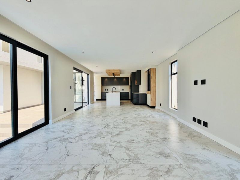 Spacious open-plan living and kitchen area featuring modern dark cabinetry, a central island, and large sliding glass doors leading to an outdoor patio.