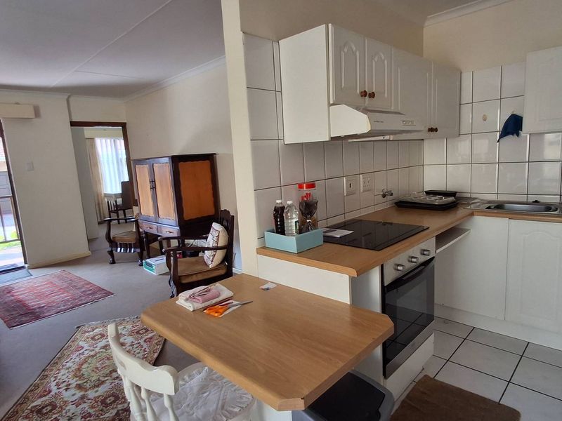 Open-plan living area featuring a functional kitchen with built-in cabinetry, electric hob, oven, and tiled splashbacks, seamlessly connected to the adjacent living space.