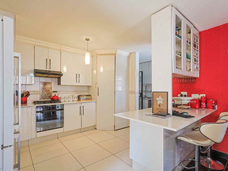 A functional kitchen featuring white cabinetry, a gas hob, an integrated oven, and a breakfast bar, with tiled flooring throughout.