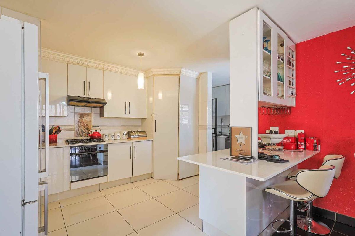 A functional kitchen featuring white cabinetry, a gas hob, an integrated oven, and a breakfast bar, with tiled flooring throughout.
