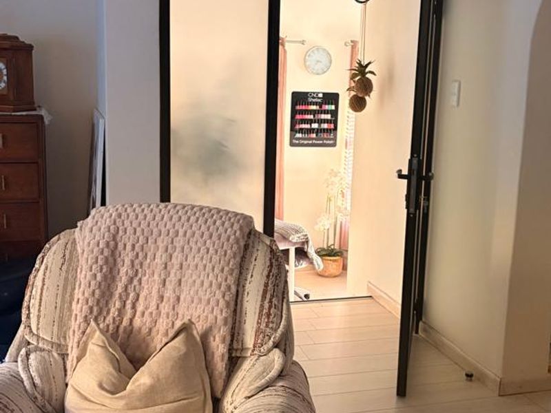 A bright living area featuring light-toned laminate flooring and a modern black metal-framed glass door leading to an adjacent room.