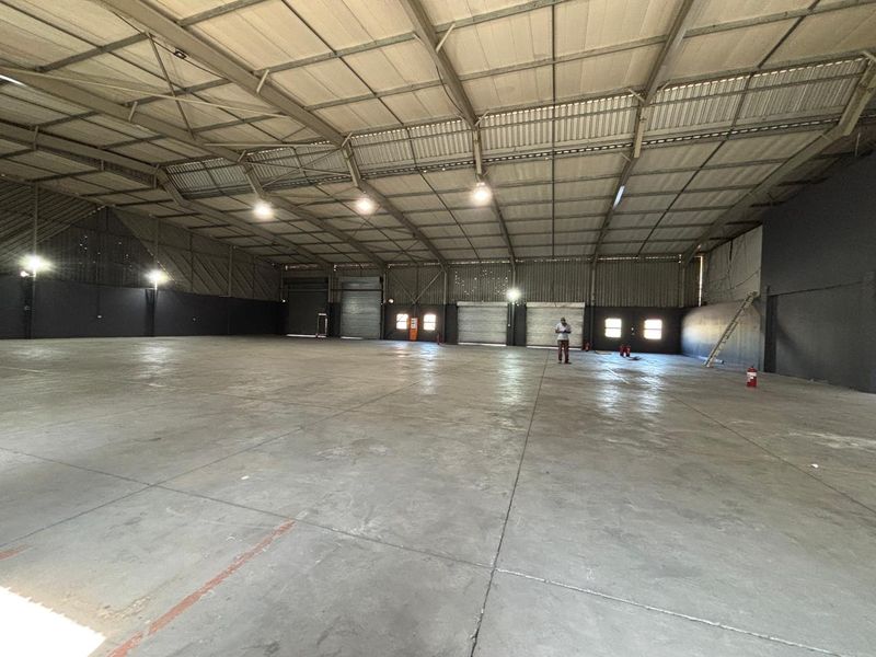 Spacious industrial warehouse featuring high ceilings, concrete flooring, and multiple roller shutter doors, suitable for storage or manufacturing operations.