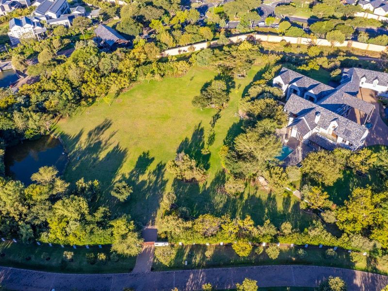 Aerial view of a large residential property featuring extensive landscaped gardens, mature trees, a swimming pool, and a paved driveway.