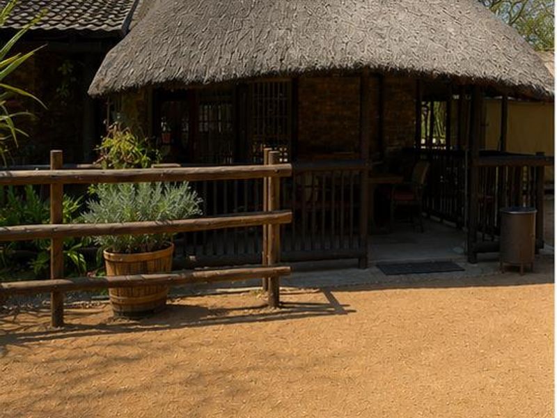 A rustic outdoor patio area featuring a traditional thatch roof and timber railing, providing a shaded space adjacent to the main house structure.