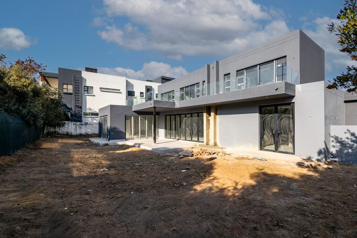 Rear view of a modern multi-story house featuring large glass sliding doors, a covered patio area, and a balcony with glass balustrades.