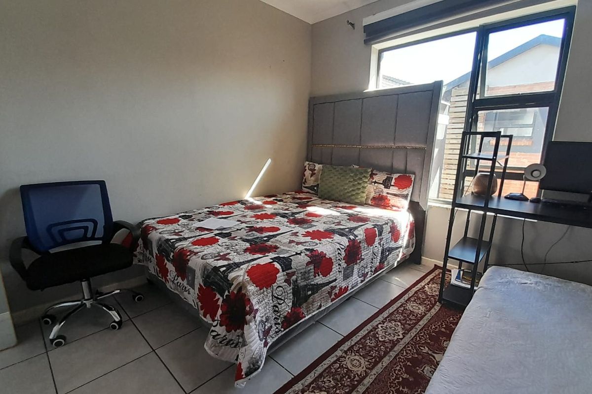 A functional bedroom featuring tiled flooring, large window with black frame, and neutral wall finishes.