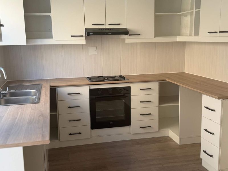 A clean, modern kitchen featuring white cabinetry, wood-look laminate countertops, a built-in oven, electric hob, and a stainless steel double sink.