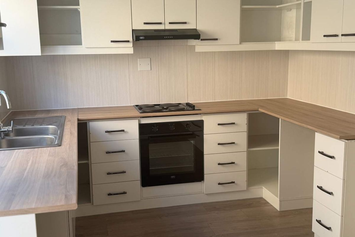 A clean, modern kitchen featuring white cabinetry, wood-look laminate countertops, a built-in oven, electric hob, and a stainless steel double sink.