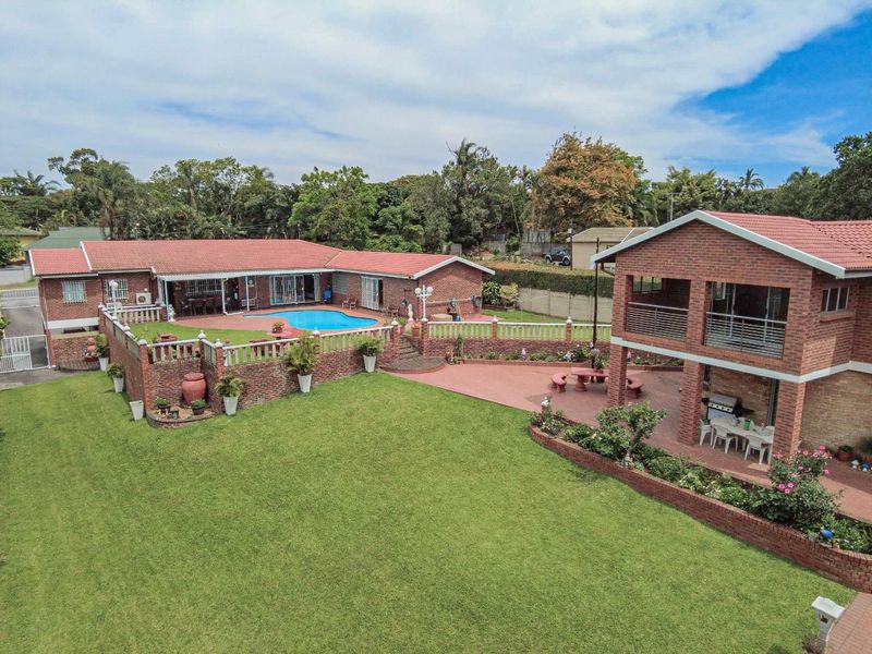 Aerial view of a residential property featuring a large lawn, swimming pool, paved patio areas, and multi-level brick structures with tiled roofing.