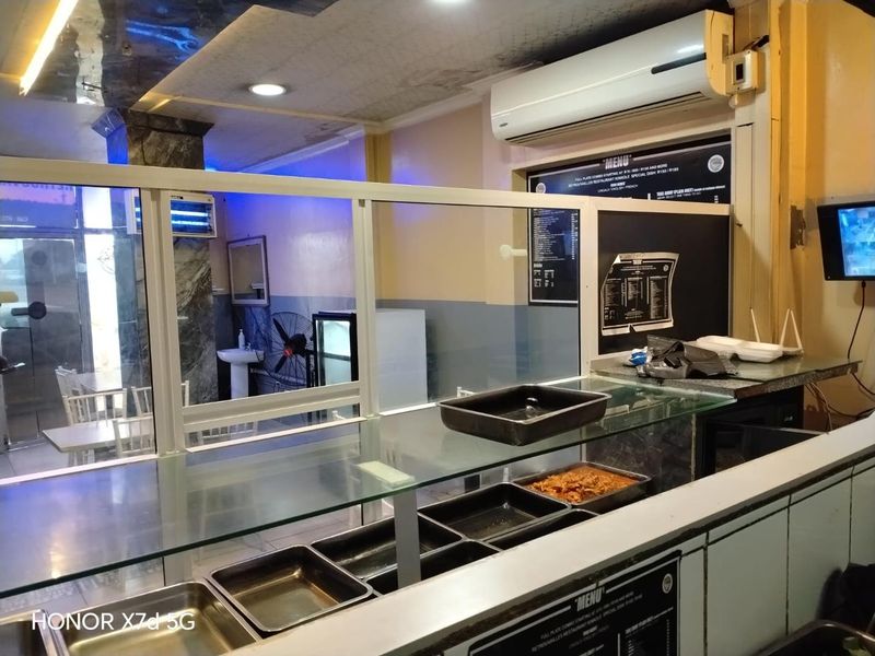 A commercial kitchen service area featuring a glass counter, wall-mounted air conditioning, and menu display boards, showing signs of wear and dated finishes.
