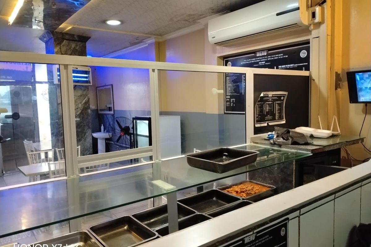 A commercial kitchen service area featuring a glass counter, wall-mounted air conditioning, and menu display boards, showing signs of wear and dated finishes.