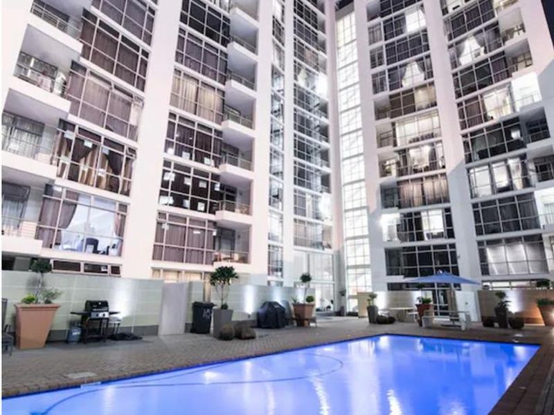 Night view of a modern high-rise penthouse complex featuring a well-maintained swimming pool and paved deck area.