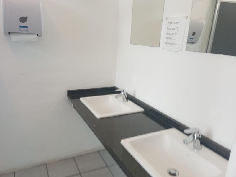 A functional office bathroom featuring a double vanity with integrated sinks, chrome faucets, and wall-mounted accessories.