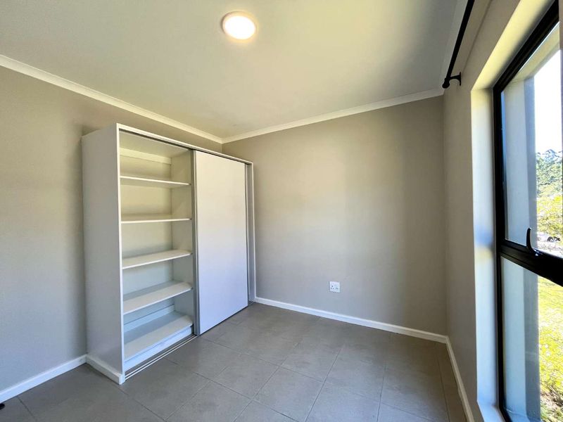 A bright, empty bedroom featuring neutral tiled flooring, a built-in sliding door wardrobe, and a large window allowing for natural light.