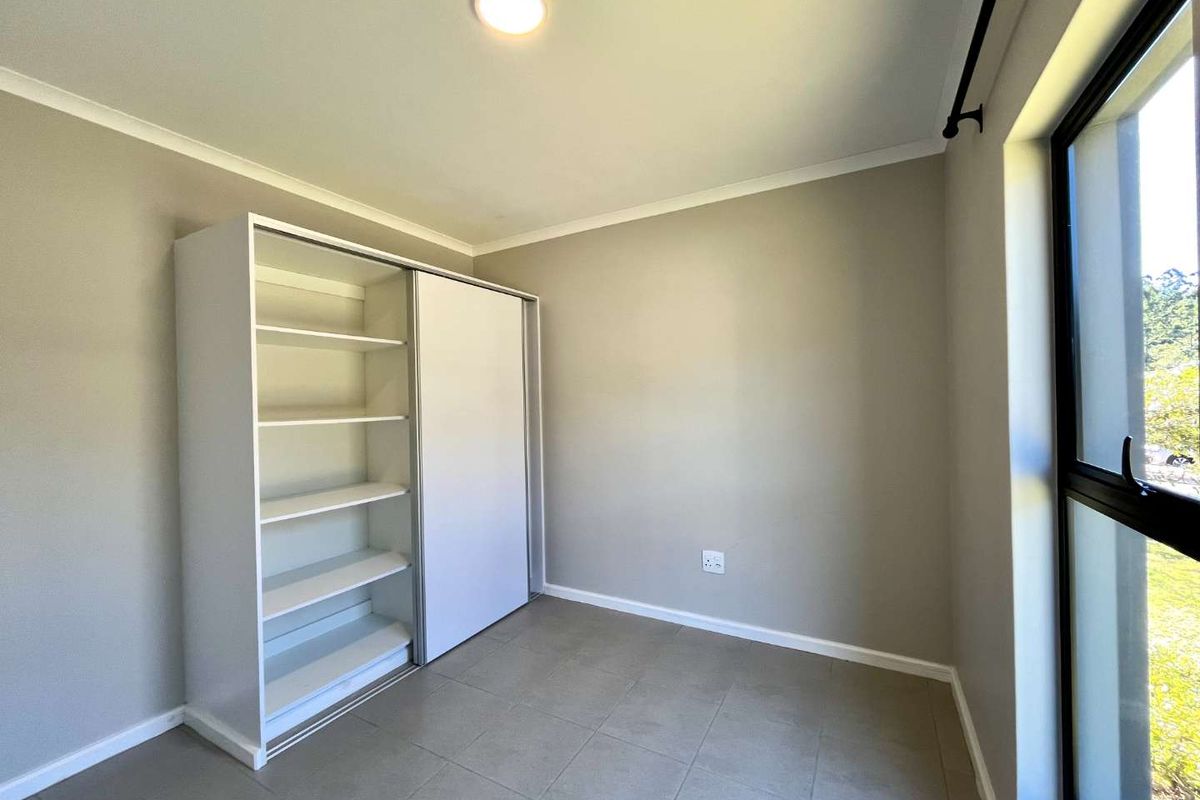 A bright, empty bedroom featuring neutral tiled flooring, a built-in sliding door wardrobe, and a large window allowing for natural light.