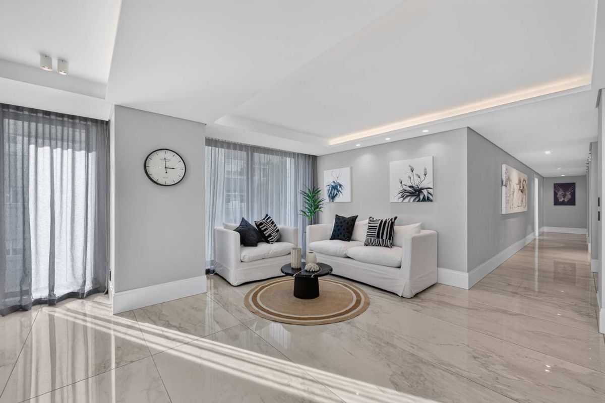 Modern living area featuring polished porcelain tile flooring, recessed ceiling lighting with cove accents, and floor-to-ceiling sheer curtains.