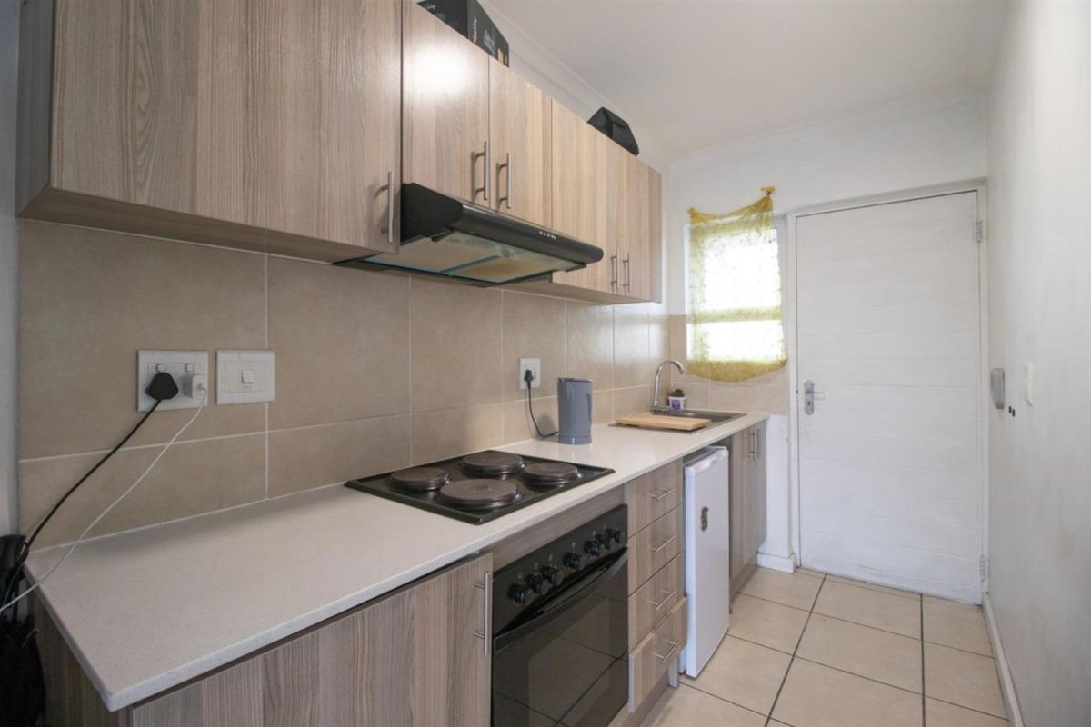 Compact kitchen featuring light wood-grain cabinetry, tiled backsplash, built-in electric hob and oven, extractor fan, and tiled flooring with direct exterior access.