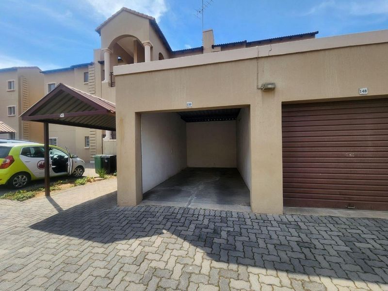 An open-fronted single garage unit with paved driveway access and an adjacent covered carport in a residential apartment complex.