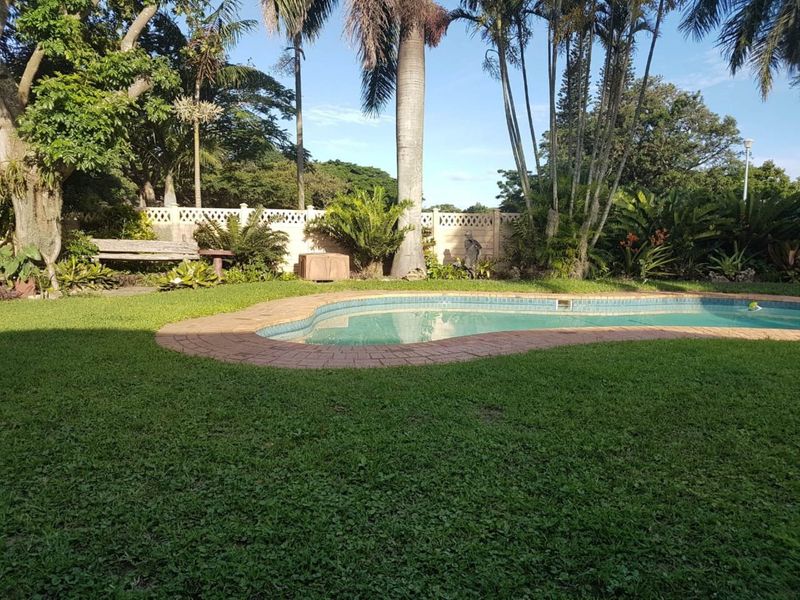 A private backyard featuring a swimming pool with brick coping, surrounded by a lush landscaped garden and a secure boundary wall.