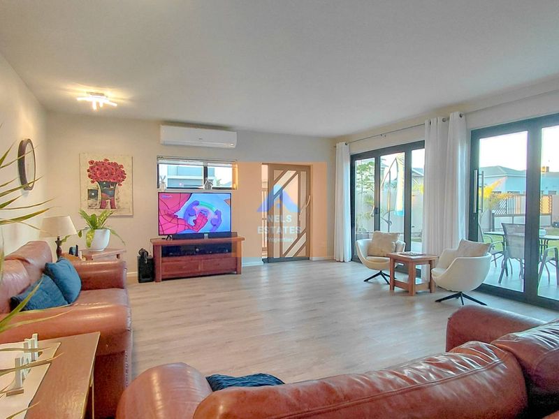 Spacious living room featuring light laminate flooring, split-system air conditioning, and large aluminium sliding doors providing seamless access to the outdoor patio and garden.