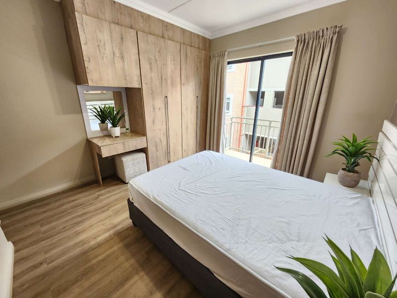 A well-maintained bedroom featuring modern wood-finish built-in cupboards with an integrated vanity and direct access to a private balcony through sliding glass doors.