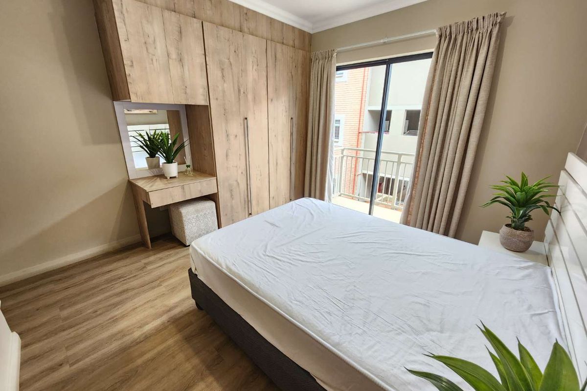 A well-maintained bedroom featuring modern wood-finish built-in cupboards with an integrated vanity and direct access to a private balcony through sliding glass doors.