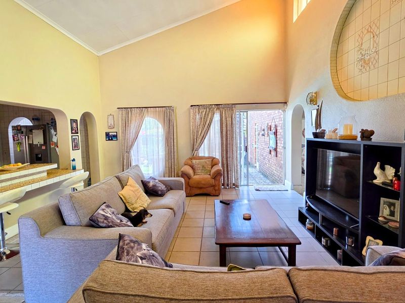 Spacious open-plan living area featuring vaulted ceilings, tiled flooring, and a breakfast bar connecting to the kitchen, with direct access to the patio.