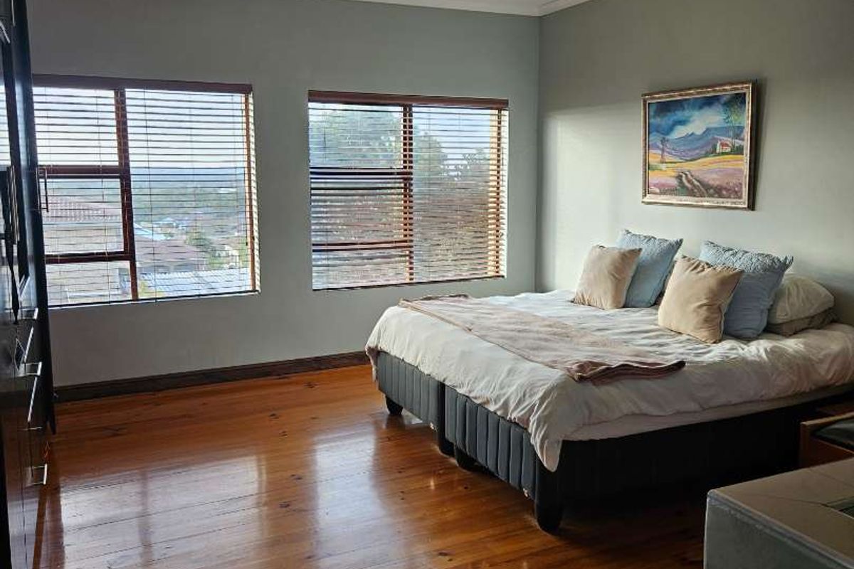Spacious bedroom featuring polished hardwood flooring, large windows with fitted blinds, and neutral wall tones, offering a bright and comfortable living space.