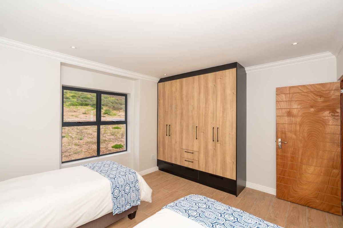 A bright bedroom featuring modern wood-grain built-in cupboards, tiled flooring, and a large window with natural views.