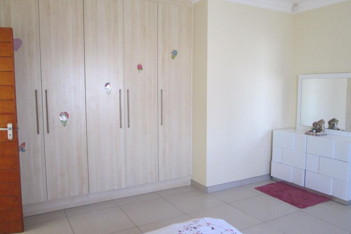A bedroom featuring light wood-finish built-in cupboards, tiled flooring, and neutral wall tones.
