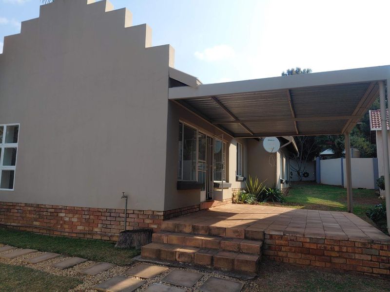 Rear view of the house featuring a covered patio area with brick steps, a stepped gable wall, and a well-maintained garden space.